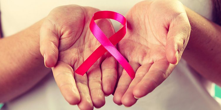 Healthcare and medicine concept - woman showing pink breast cancer awareness ribbon on hands, closeup